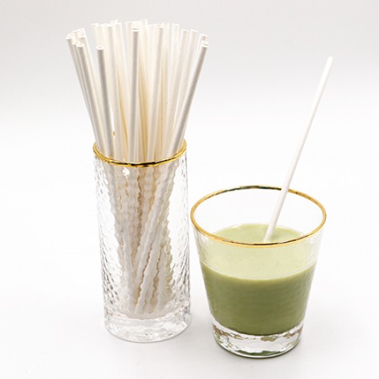 Glass Filled with White Paper Straws and a Glass of Green Juice Beside it with a White Straw in it.